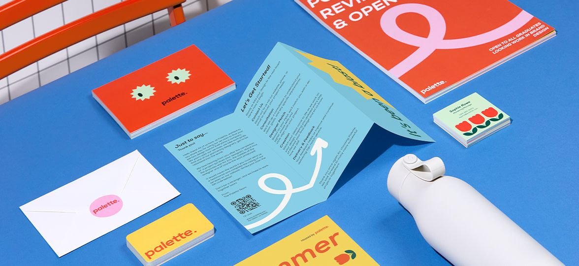 lat lay of vibrant, colorful stationery designs including folded brochures, business cards, and an envelope on a bright blue background.